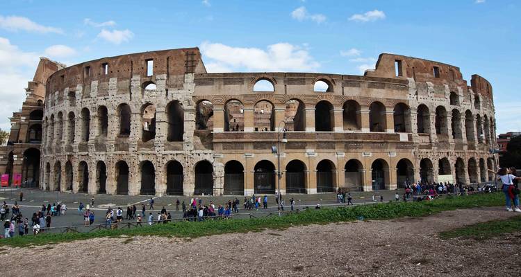 The exterior of the Colosseum rises against a bright blue sky while crowds gather at its base.