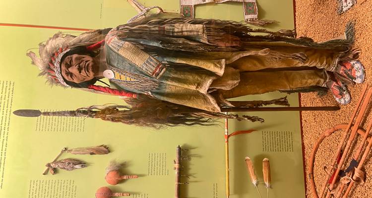 Figurine autochtone réaliste tenant une lance dans une exposition muséale d'artefacts.