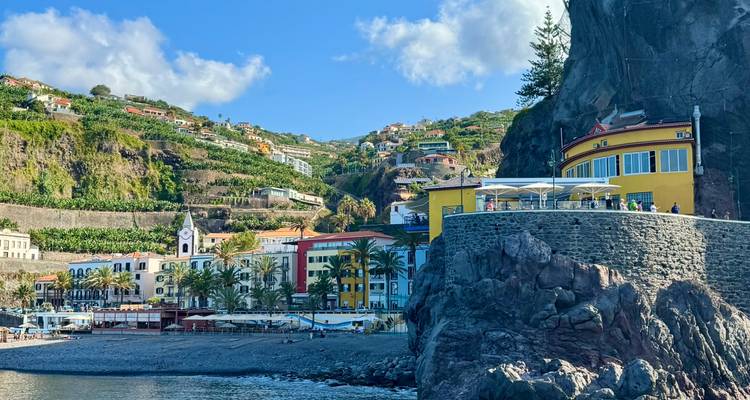 Colorful seaside village with a yellow building perched on a rocky promontory beside calm bay waters