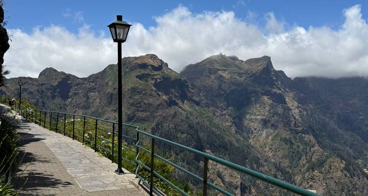 Paved mountain walkway with classic lamp posts leading to a panoramic viewpoint over rugged peaks and clouds