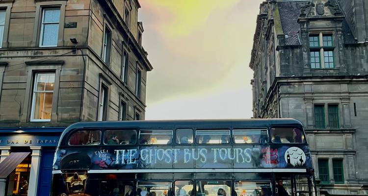 Bus fantôme à deux étages de couleur noire garé entre des bâtiments historiques en pierre au coucher du soleil.