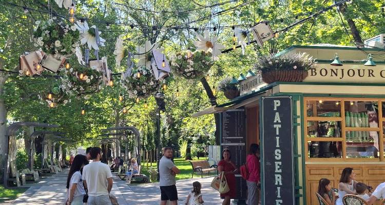 Parc piétonnier animé avec des décorations florales suspendues au-dessus d'un kiosque de pâtisserie où les gens se détendent sur des bancs.