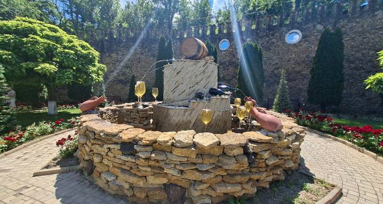 Fontaine en pierre rustique avec tonneau de vin et verres de champagne dans une cour ensoleillée de cave vinicole.