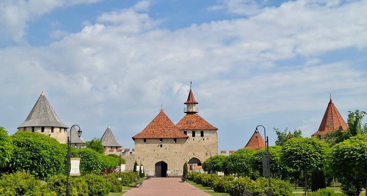 Forteresse historique en pierre dotée de plusieurs tours coniques entourée de jardins paysagers luxuriants.