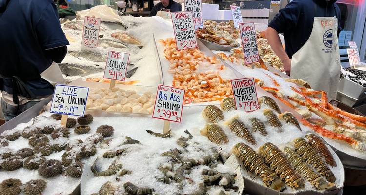 Étal de marché aux fruits de mer recouvert de glaçe, garni de crevettes, de queues de homard et de pancartes de prix manuscrites.