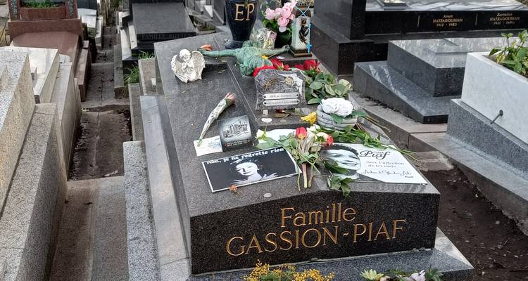 Ornate gravesite of Edith Piaf with flowers, photos and memorial items in a Paris cemetery.