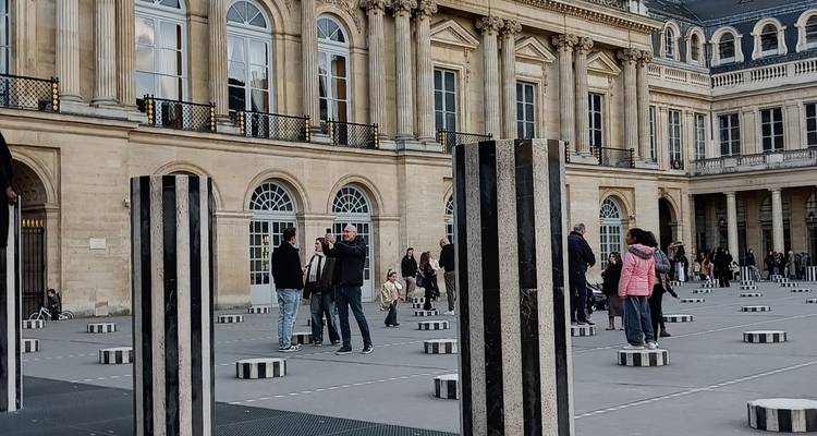 Modern striped columns installation in the Palais Royal courtyard with visitors exploring the artwork.