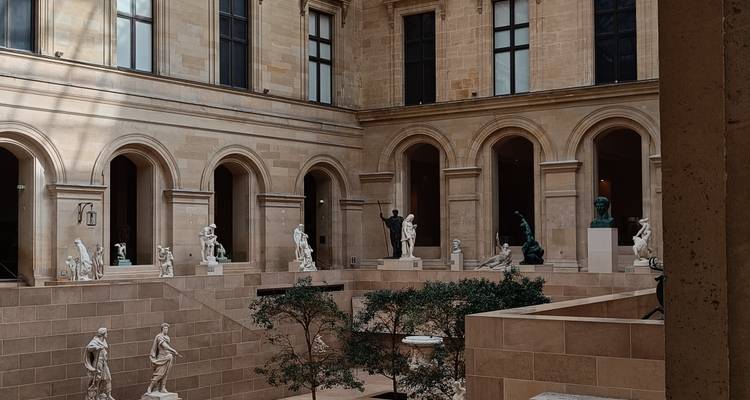 Elegant interior courtyard of the Louvre with classical statues displayed under high stone arches.