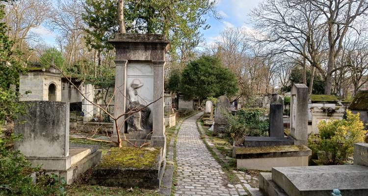 Peaceful cobblestone path winding through moss-covered tombs and trees in a Paris cemetery.
