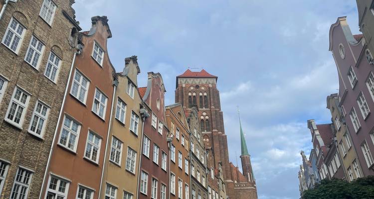 Des maisons de ville étroites et colorées menant à une imposante cathédrale en briques rouges sous un ciel partiellement nuageux.