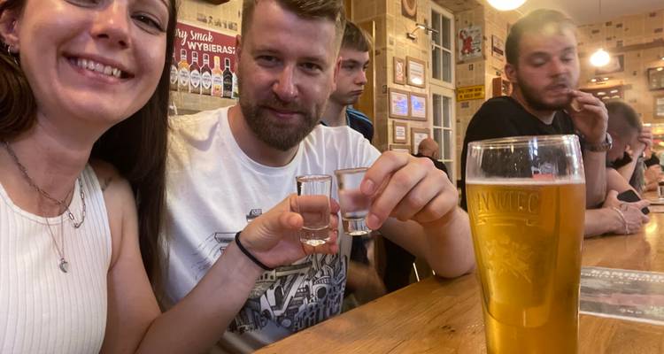 Des amis assis à un bar en bois levant des verres de vodka et une pinte de bière dans un pub douillet.