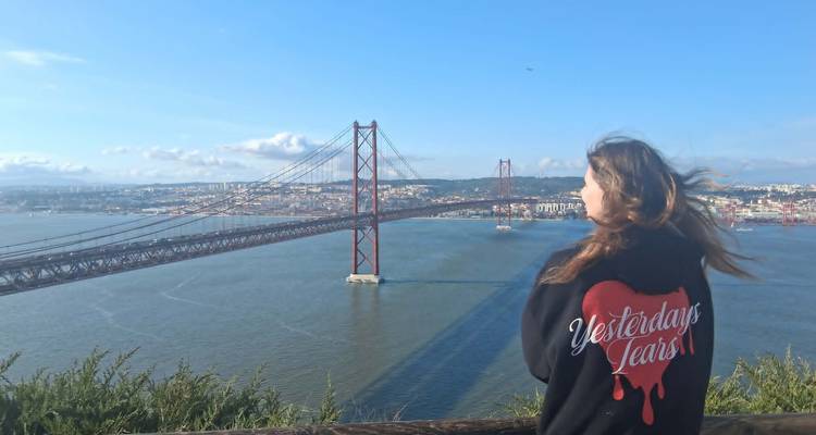 Woman with wind-blown hair overlooking 25 de Abril Bridge and Tagus River from viewpoint.