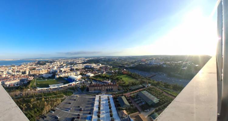 Wide aerial panorama of Lisbon city and coastal plain under bright sun with long shadows.