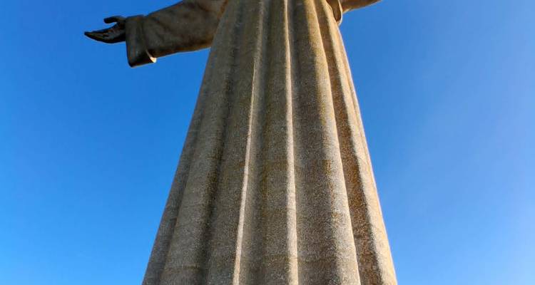Upward angle of giant stone Cristo Rei statue against clear deep blue sky.