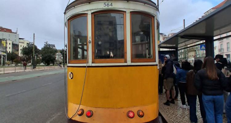 Iconic yellow vintage tram stopped at city shelter with passengers boarding.