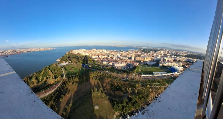 Panoramic bird's-eye view of Lisbon and Tagus River under clear sky from high observation deck.