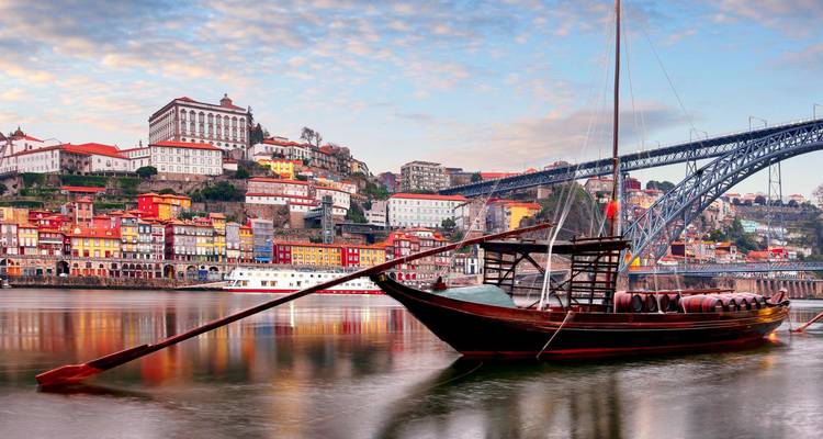 Bateau rabelo traditionnel amarré sur le fleuve Douro avec le front de mer coloré de Porto et le pont Dom Luís I en arrière-plan.