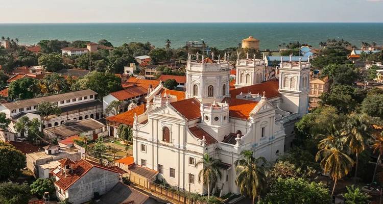 Aerial view of a large white colonial-era church with red-tiled roof surrounded by palms and the Indian Ocean backdrop in Sri Lanka.