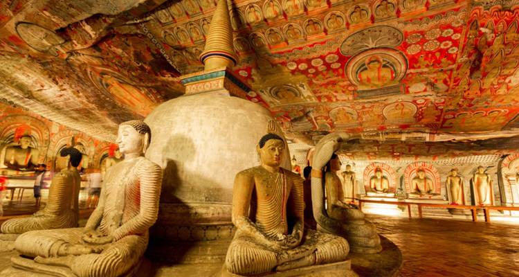 Interior of Dambulla Cave Temple filled with richly painted ceilings, a central stupa and seated Buddha statues.