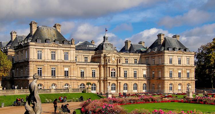 Elegant Luxembourg Palace surrounded by colourful flower gardens under patchy clouds.