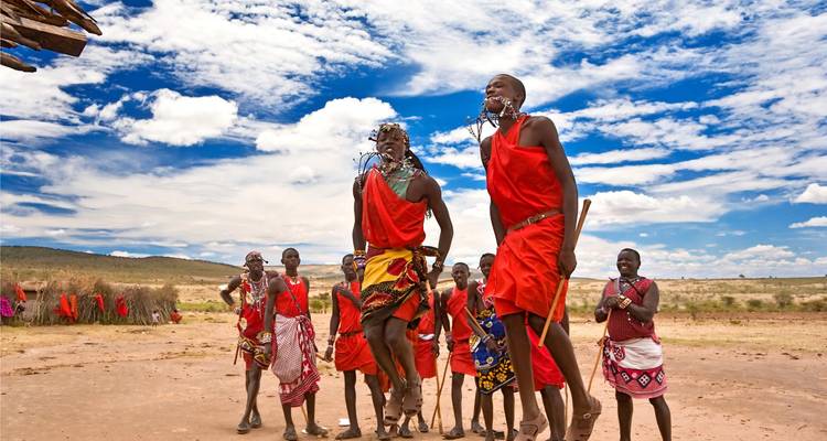 Des hommes Maasaï vêtus de rouge exécutant une danse de saut en hauteur sous un ciel bleu éclatant.
