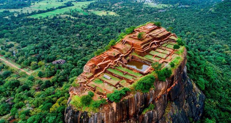 Dramatic drone view of Sigiriya fortress ruins perched atop a towering rocky monolith amid dense jungle.