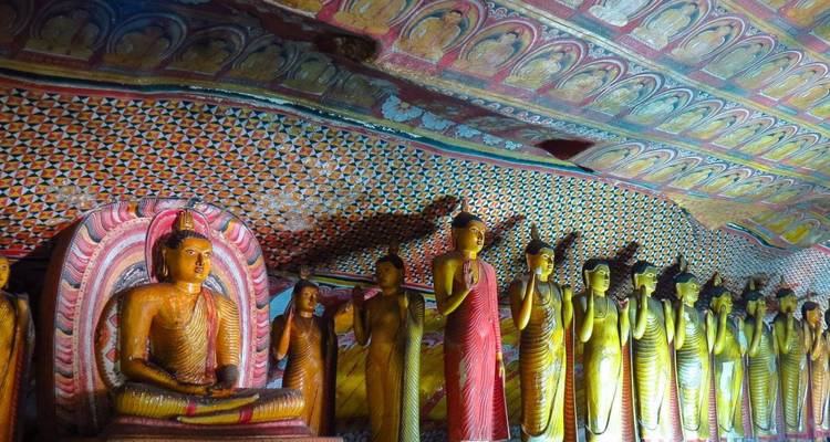 Row of vividly painted Buddha statues lining the wall of Dambulla Cave Temple.