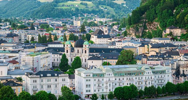 Vue panoramique de Salzbourg avec des collines verdoyantes, des clochers d'églises et une architecture variée sous une lumière douce.