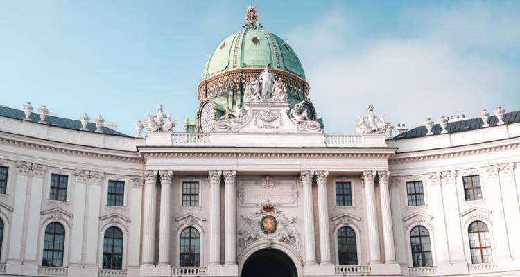 Le dôme vert en cuivre ouvragé et la façade néoclassique du Palais de la Hofburg de Vienne sous une douce lumière matinale.
