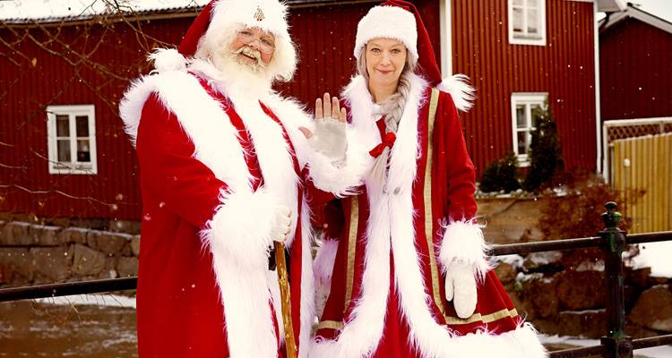 Un Père Noël jovial et une Mère Noël en costumes rouges traditionnels faisant des gestes d'adieu parmi les flocons de neige qui tombent.