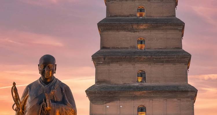 La statue d'un moine bouddhiste se dresse devant l'ancienne Grande Pagode de l'Oie Sauvage au coucher du soleil à Xi'an.