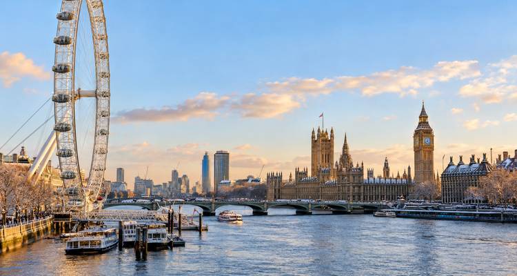 Iconic London skyline at golden hour with London Eye, Houses of Parliament and boats on the Thames.