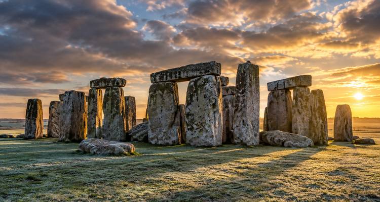 Sunrise light casting long shadows across the ancient stone circles of Stonehenge.