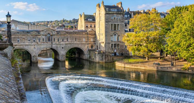 Picturesque Pulteney Bridge and cascading weir on the River Avon in Bath under bright blue sky.