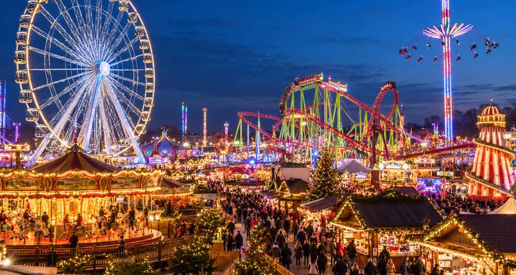 Colorful night-time funfair packed with lights, a giant Ferris wheel, roller-coasters and crowds enjoying the attractions.