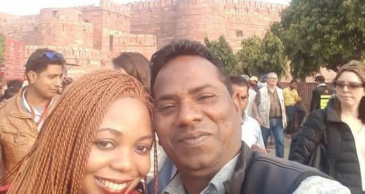 Selfie rapproché d'un couple de touristes avec les murs du Fort d'Agra et d'autres visiteurs en arrière-plan.