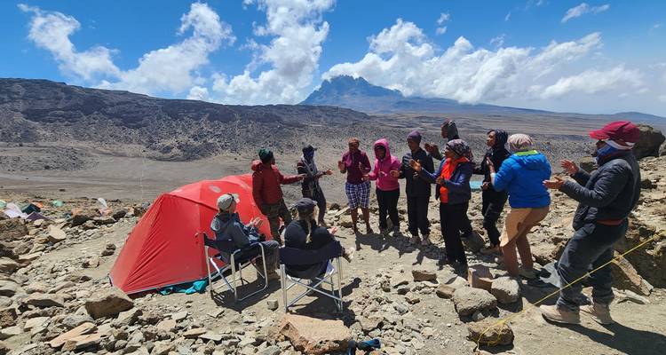 Des campeurs célèbrent et dansent près d'une tente rouge dans le paysage rocheux d'haute altitude du Kilimandjaro.
