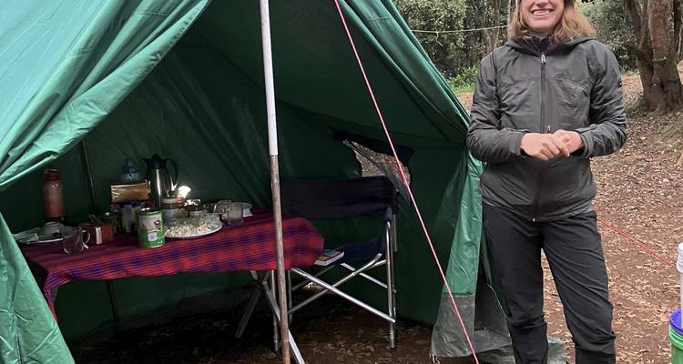 Un trekkeur souriant se tient à l'entrée d'une tente-restaurant verte dans un camp forestier.