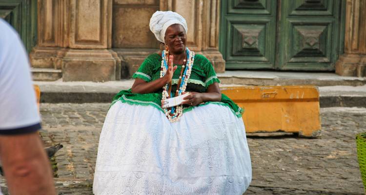 Frau in traditioneller Baiana-Kleidung begrüßt Besucher vor einer Barockkirchenfassade.