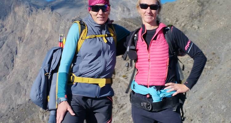 Deux trekkers souriants pour la caméra sur un sentier montagneux avec des falaises escarpées dans la douce lumière du matin.