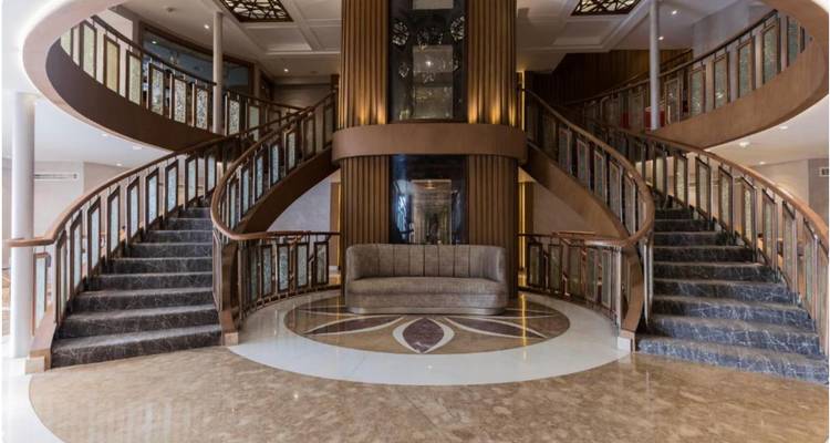 Un élégant double escalier avec des sols en marbre et des rampes décoratives à l'intérieur du foyer d'un navire de croisière.
