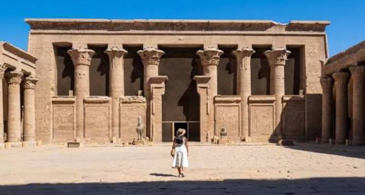 Un visiteur solitaire se tient dans la grande cour du Temple d'Horus, entouré de colonnes de pierre imposantes.