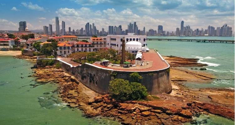 Historic fortifications of Casco Viejo jutting into green water with Panama City’s modern skyscraper skyline behind.