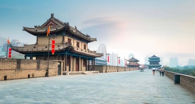 Allée pavée de pierre au sommet de l'ancienne muraille de Xi'an avec tours de porte et promeneurs flous.