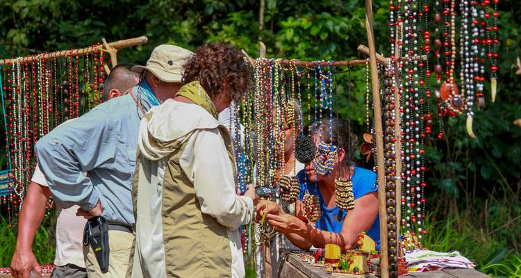 Les voyageurs parcourent les bijoux de perles faits à la main aux couleurs vives dans un étal de marché rustique en pleine jungle.