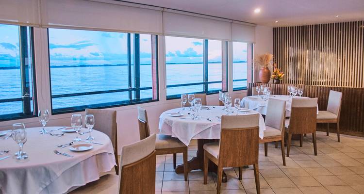 Salle à manger élégante sur un bateau fluvial avec des baies vitrées panoramiques donnant sur des eaux calmes au crépuscule.