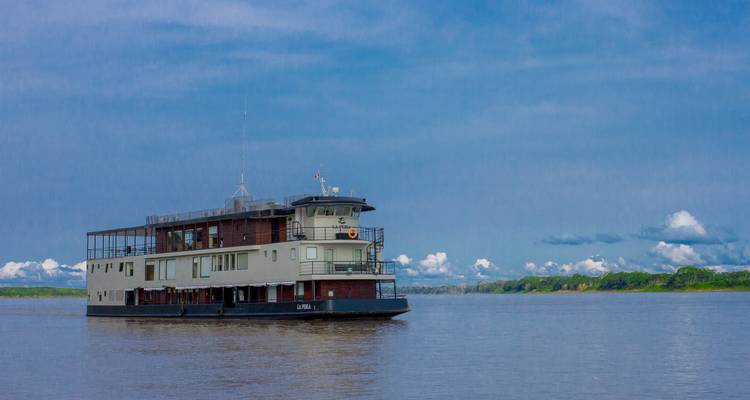 Un navire de croisière fluviale moderne à plusieurs ponts navigue sur un large affluent de l'Amazone sous un ciel bleu éclatant.