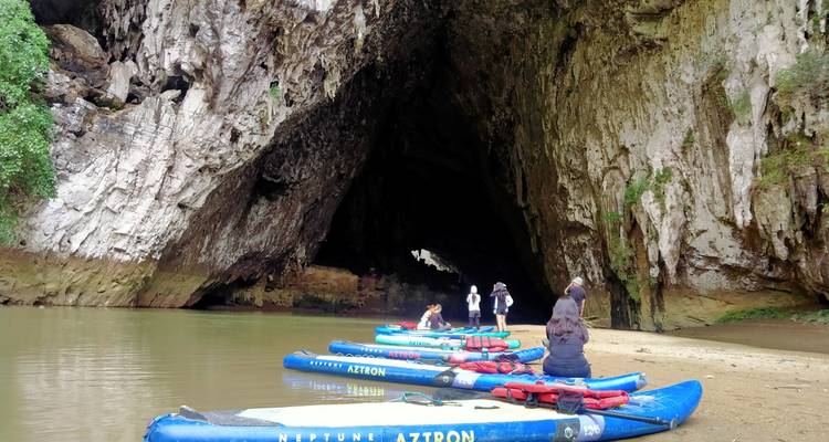 Las tablas SUP inflables azules descansan en una orilla arenosa en la boca abierta de una cueva de piedra caliza mientras los palistas se preparan.