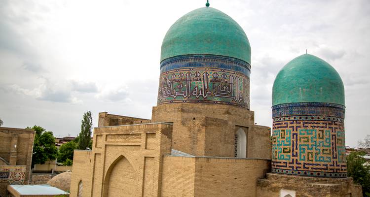Twin turquoise-tiled domes decorated with Islamic calligraphy rise above an ancient brick madrasa.
