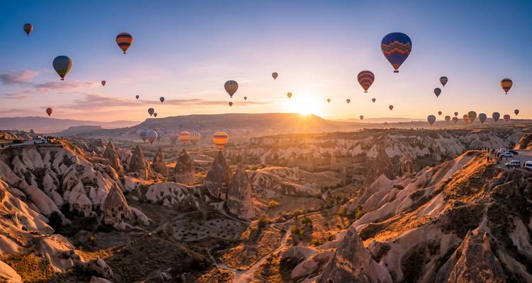 Dozens of colourful hot-air balloons rise over Cappadocia’s jagged rock valleys at sunrise.